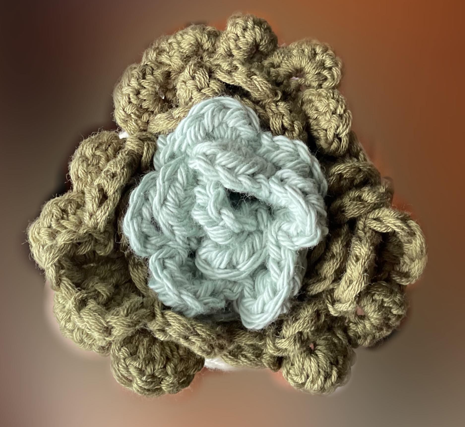 A close up of a crocheted flower on a blurry brown background