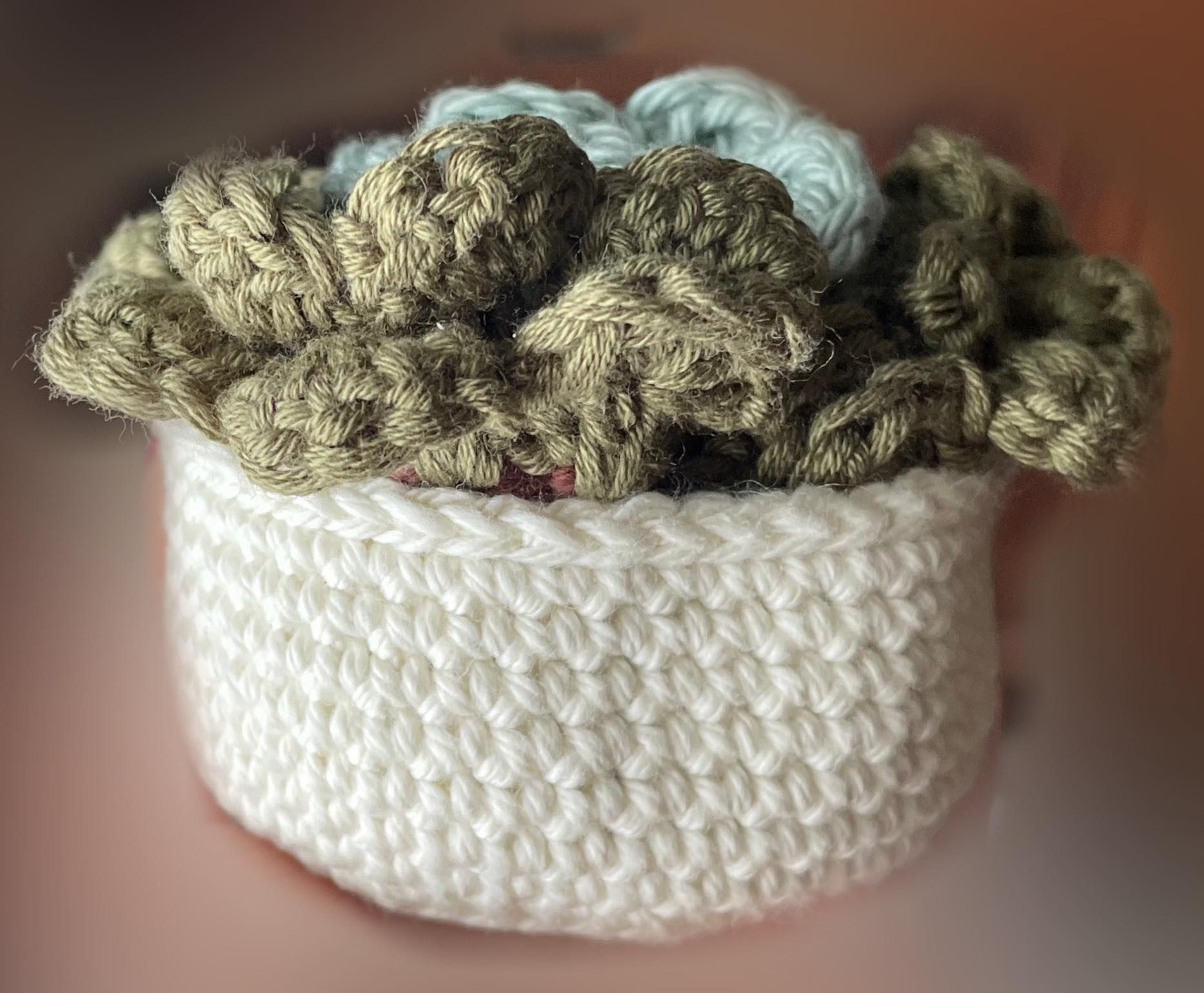 A white hand crocheted pot filled with hand crocheted drink coasters that resemble flowers.