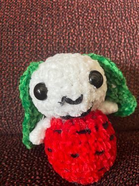 A stuffed animal that looks like a strawberry with green ears is sitting on a couch.