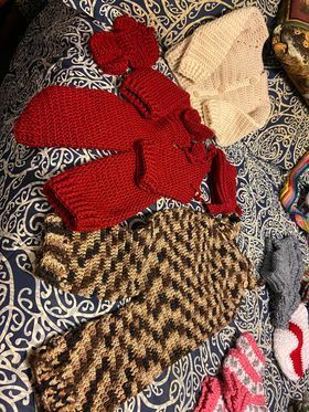 A bunch of knitted clothes are laying on a bed.