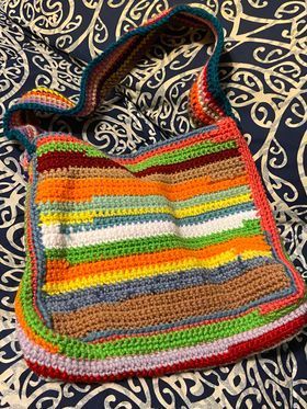 A colorful crocheted bag is sitting on top of a bed.
