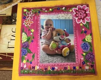 A picture of a baby sitting next to a stuffed animal in a pink frame.