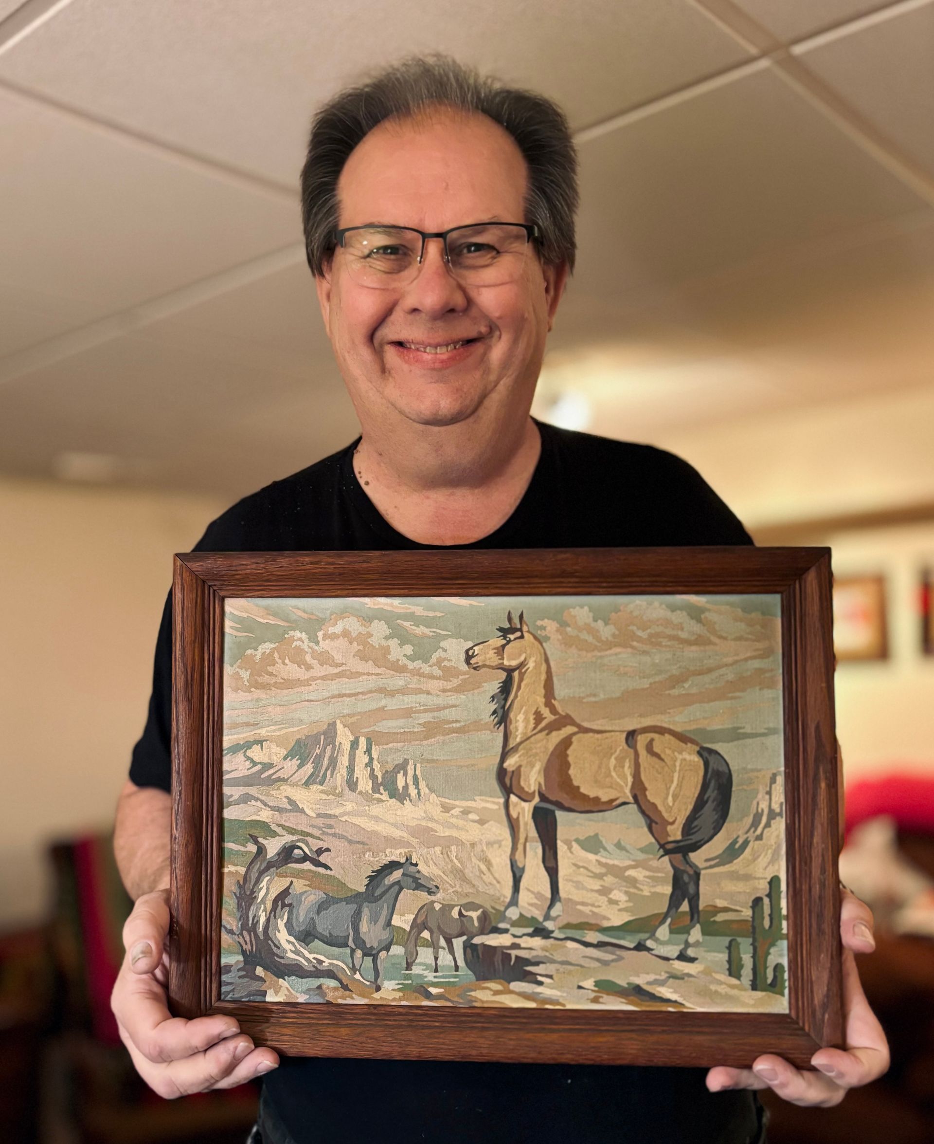 A man is holding a framed painting of a horse