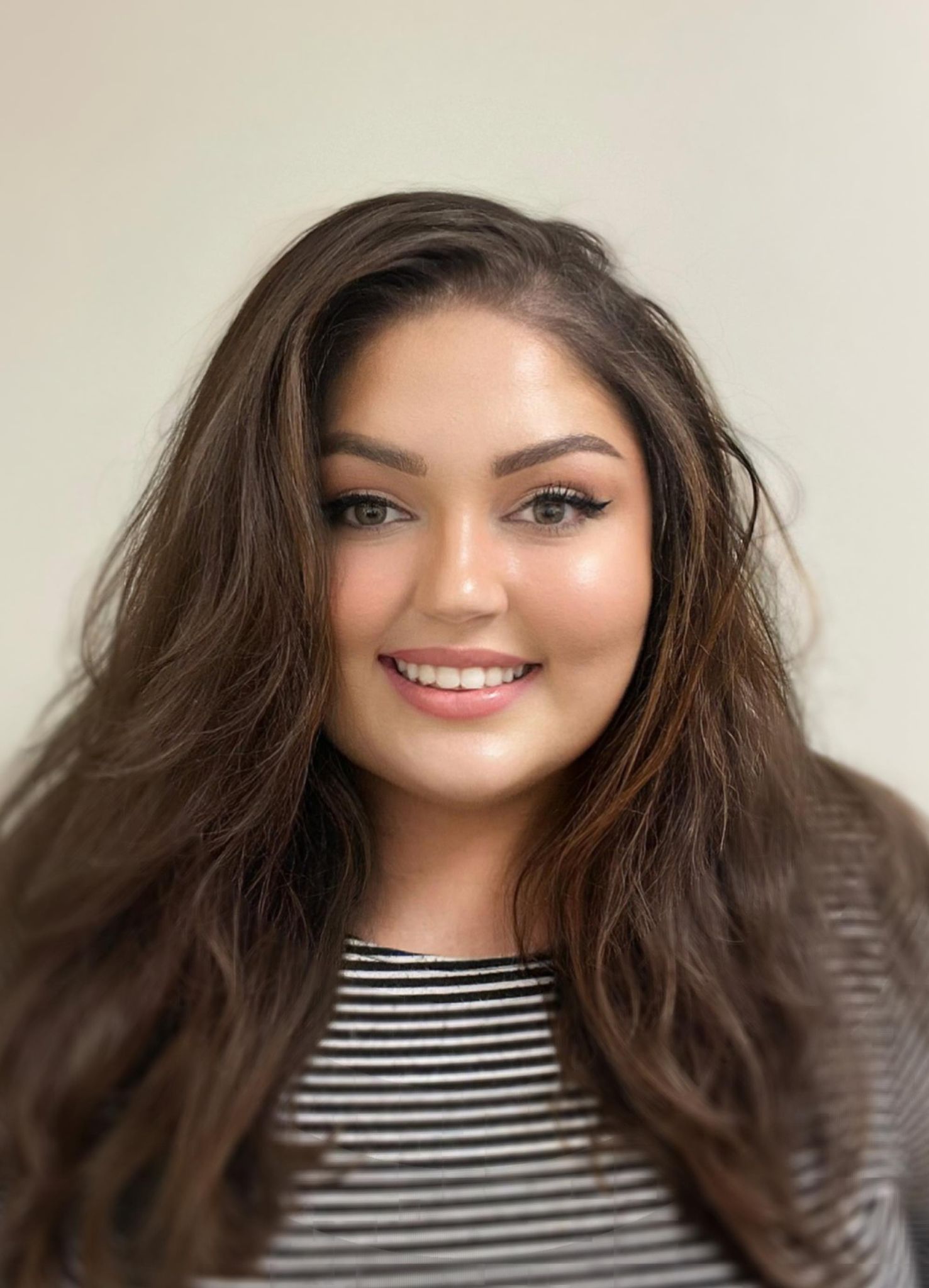 A woman with long brown hair is wearing a striped shirt and smiling.