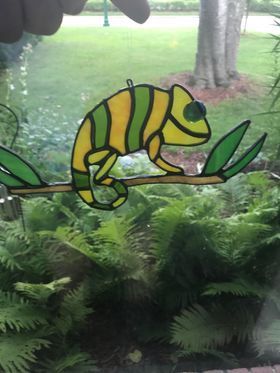 A stained glass chameleon is sitting on a branch in a garden.
