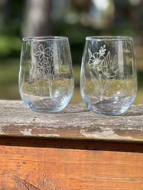 Two wine glasses with flowers on them are sitting on a wooden table.