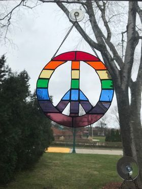 A stained glass peace sign is hanging from a tree