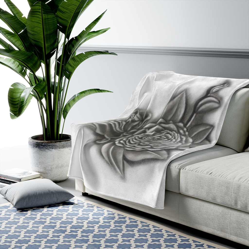 A couch with a white blanket with a black and white flower drawing on it and a plant in the background.