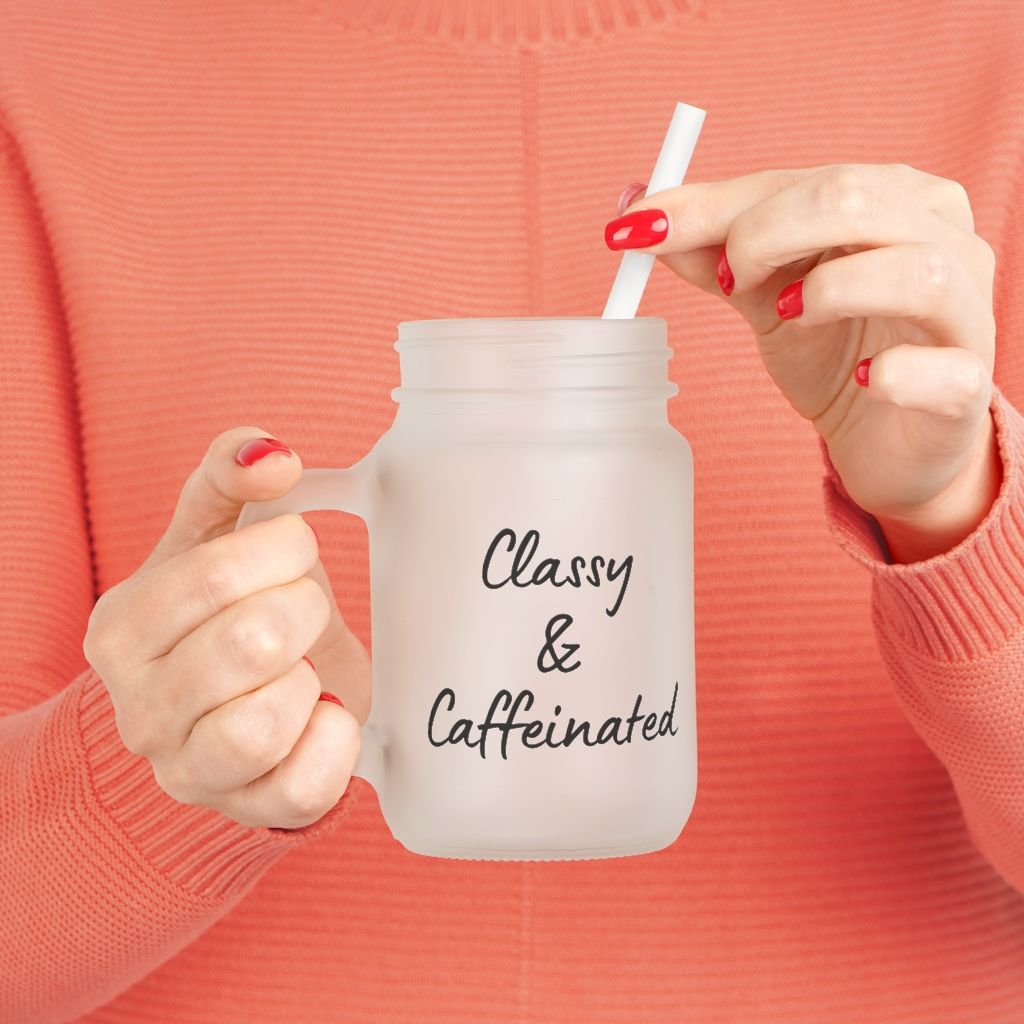 A woman is holding a mason jar with a straw that says classy and caffeinated