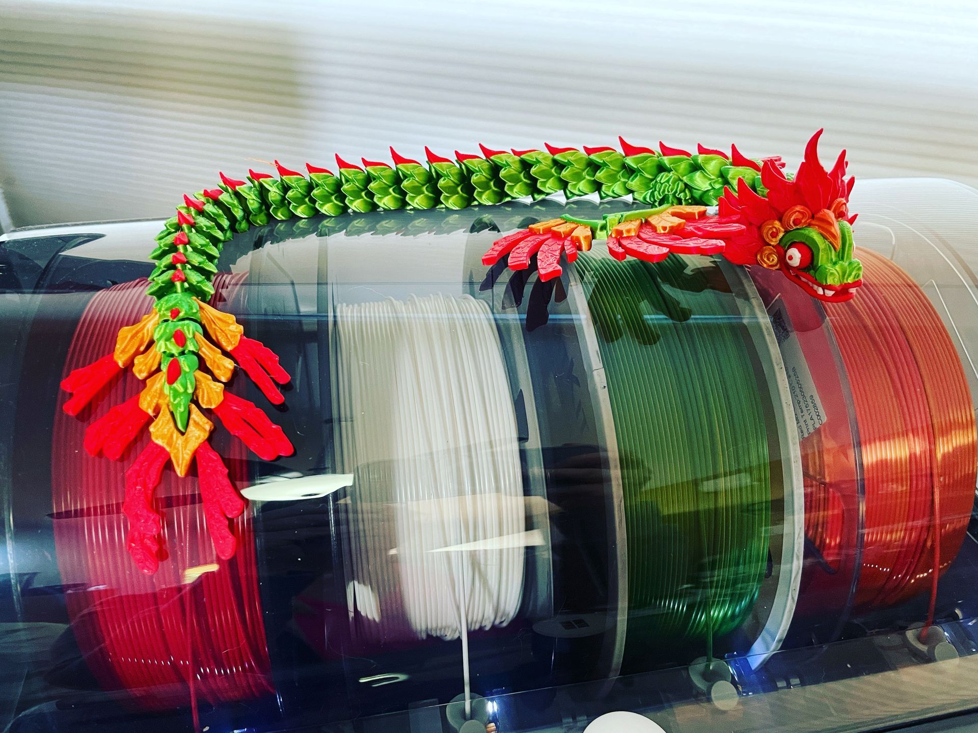 A toy dragon is sitting on top of a spool of yarn