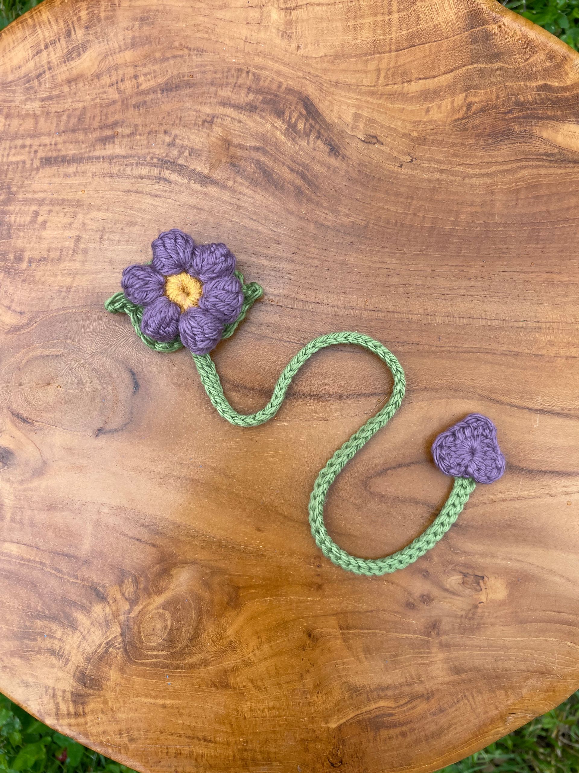 Two green crocheted leaves are sitting on top of a wooden cutting board.