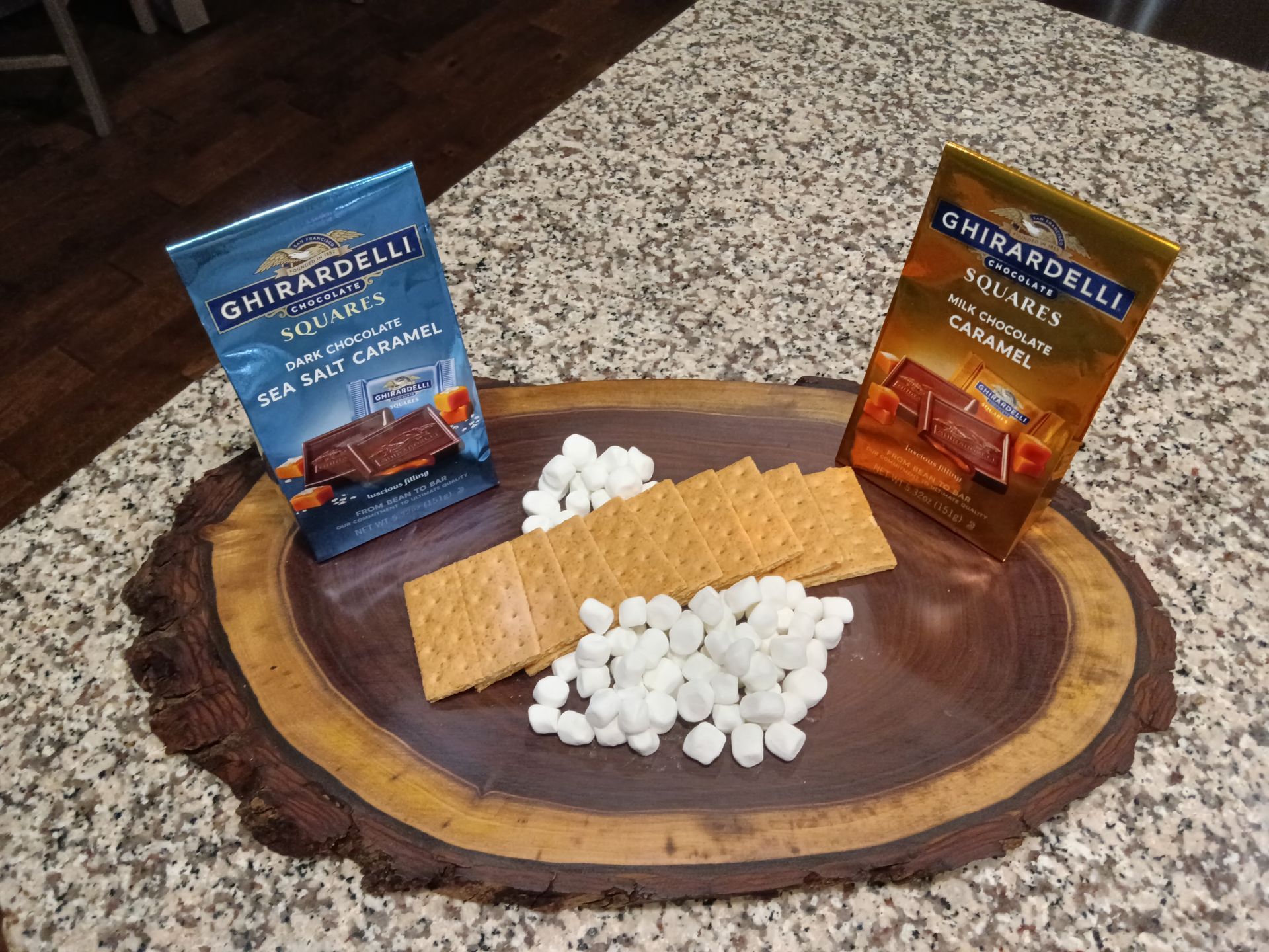A wooden plate topped with graham crackers and marshmallows on a counter.