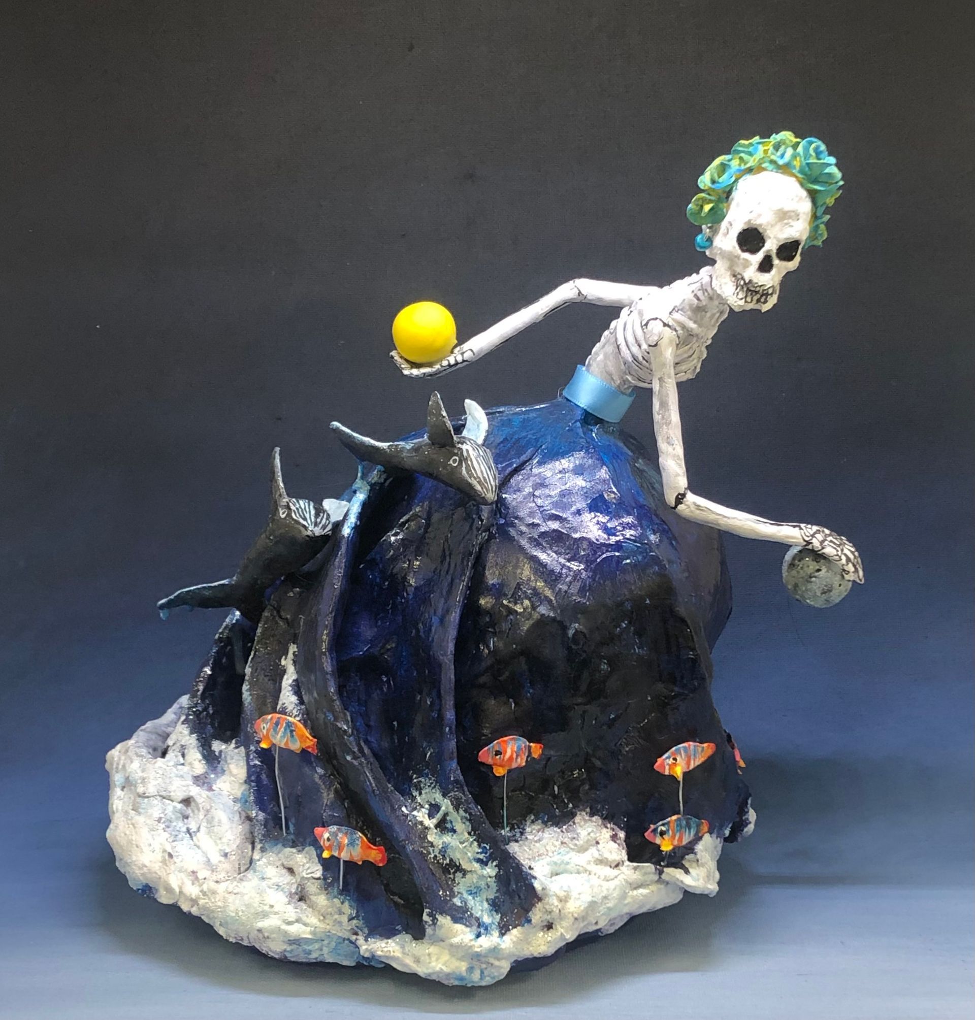 A statue of a skeleton in a blue dress holding a yellow ball
