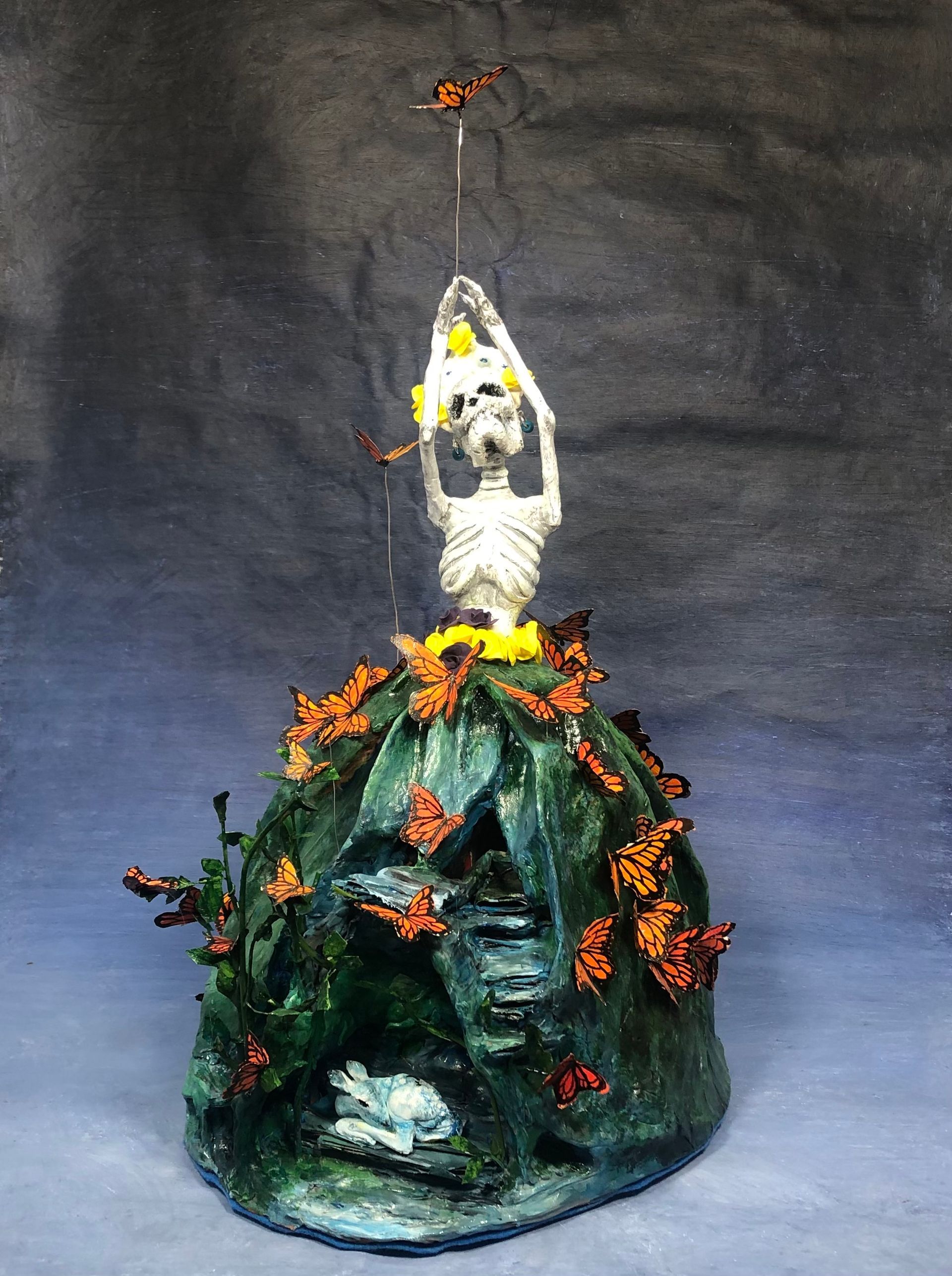 A statue of a skeleton sitting on top of a rock surrounded by butterflies.