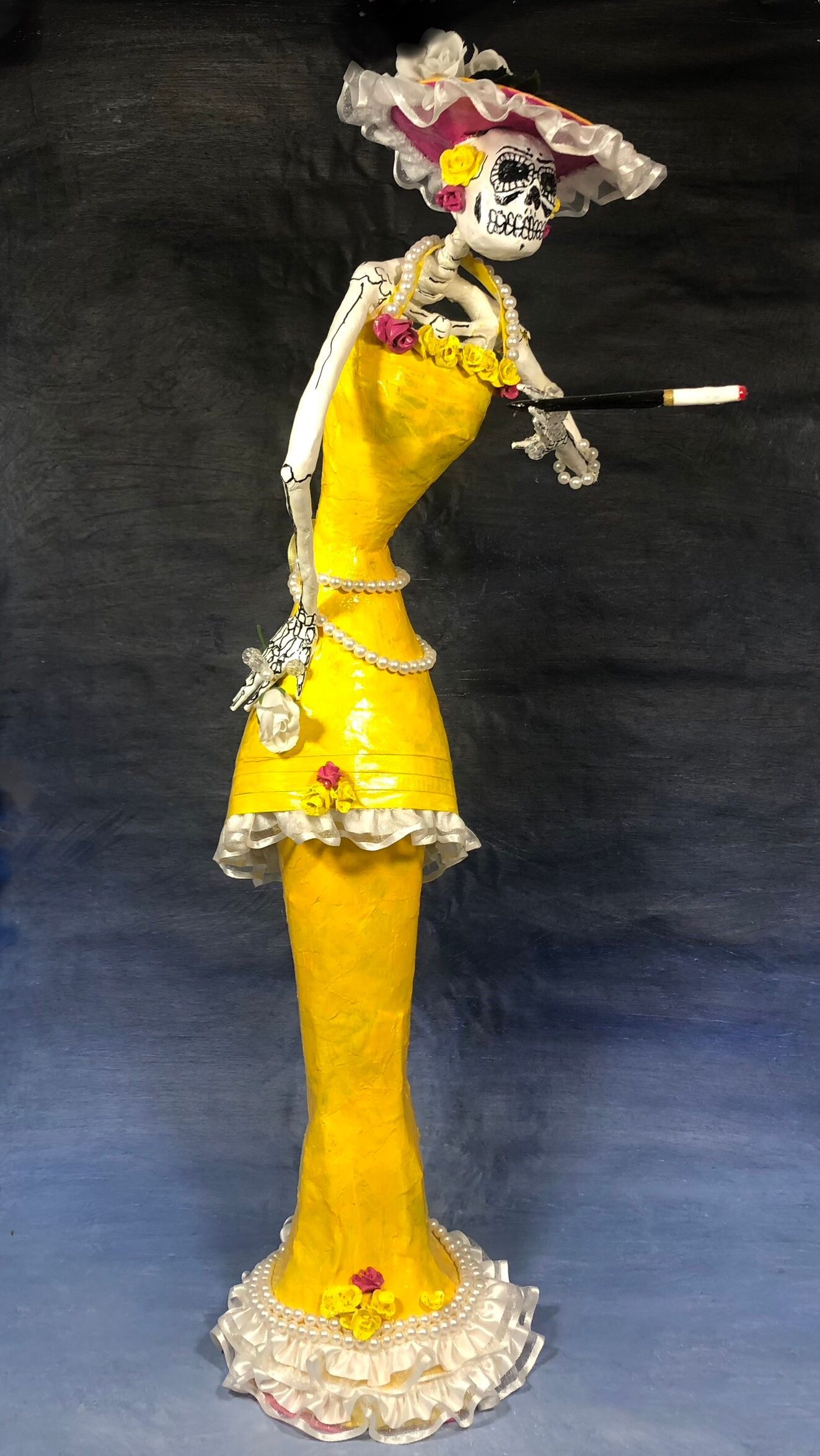 A handmade figurine of a skeleton in a vintage style yellow dress holding a yellow ball
