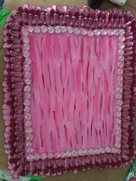 A pink tray with a pink border made from foam and pinecones is sitting on a table.