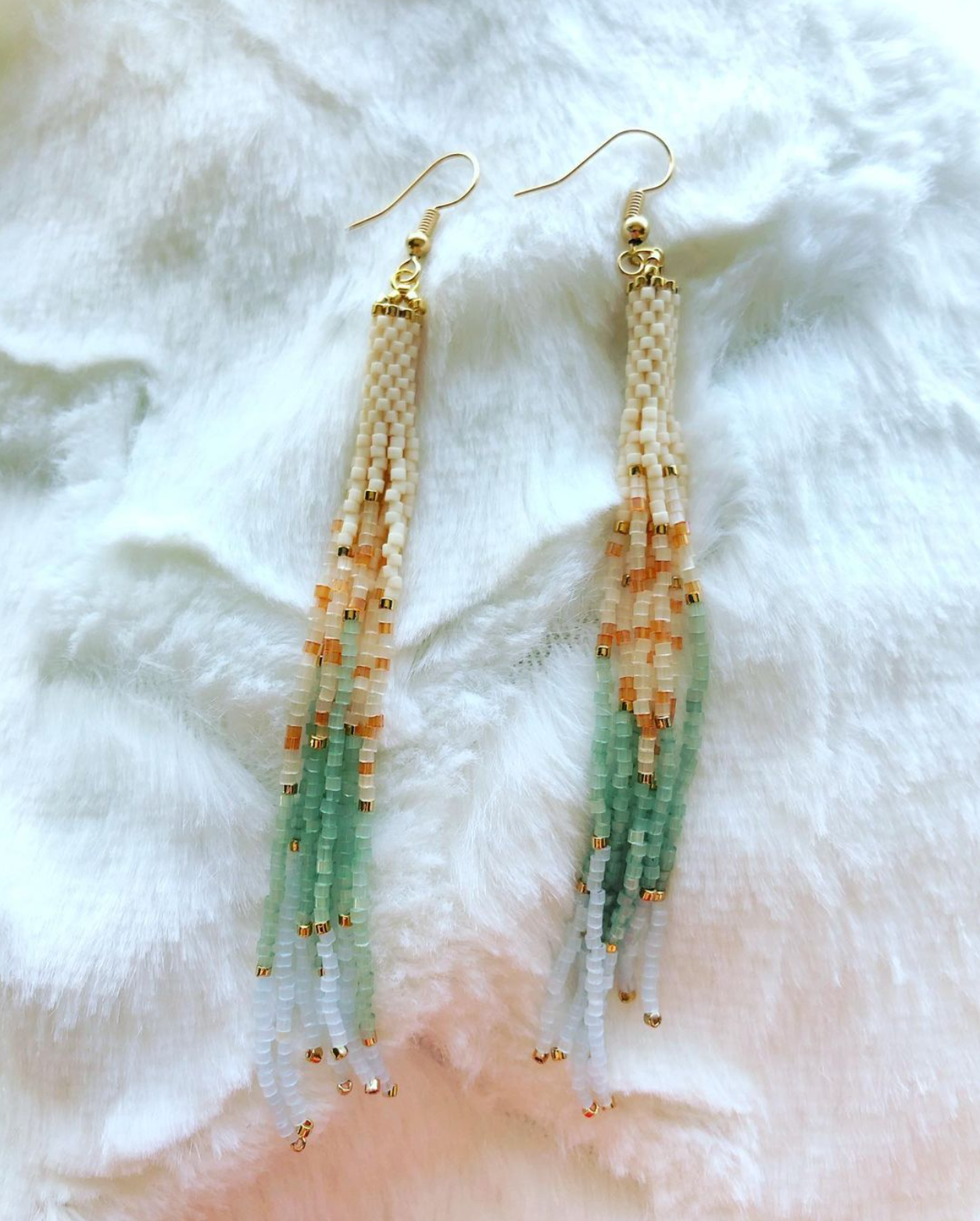 A pair of beaded earrings are sitting on a white cloth