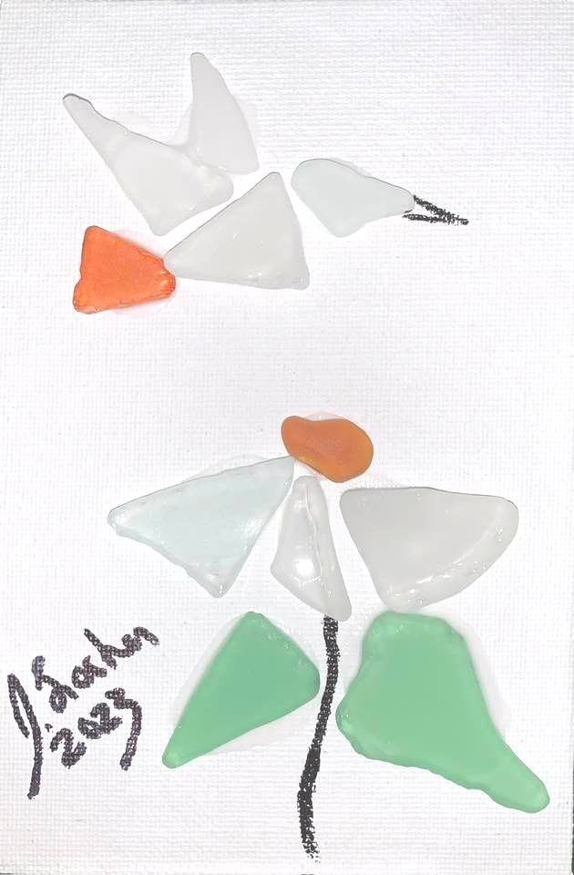 A bird is flying over a flower made of sea glass.