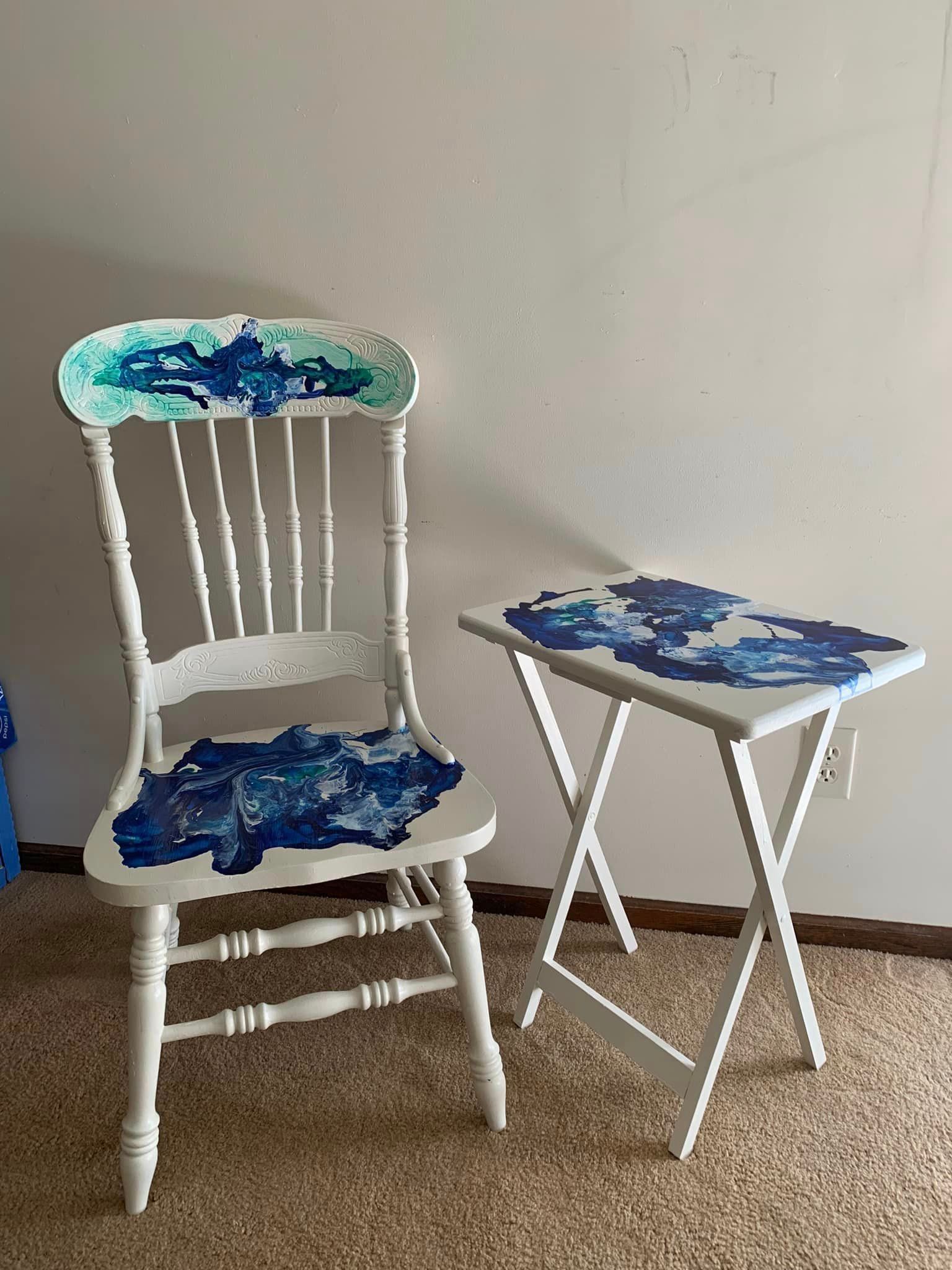 A chair and a table are sitting next to each other in a room. They have hand painted abstract designs on them.