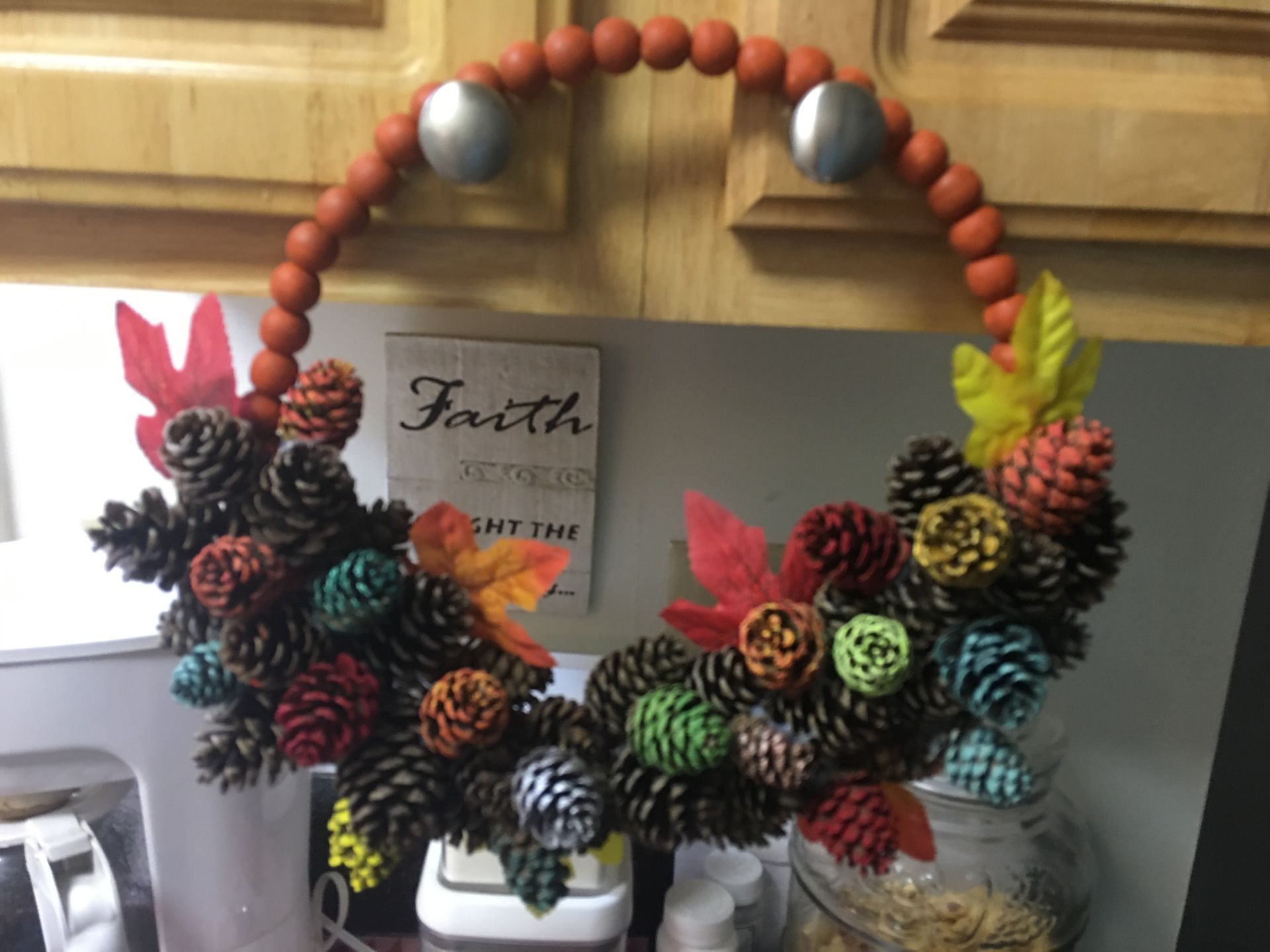 A wreath made of pine cones and beads hangs on a door