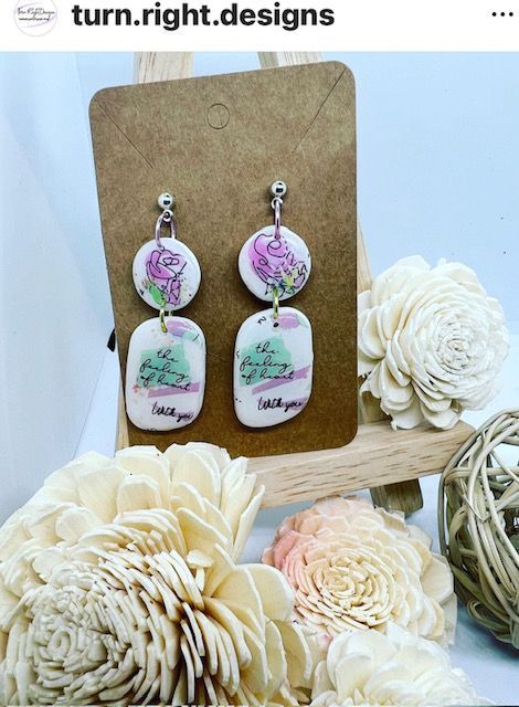 A pair of earrings sitting on top of a cardboard holder surrounded by flowers