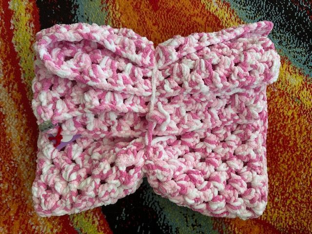 A pink and white crocheted scarf is sitting on a colorful rug.