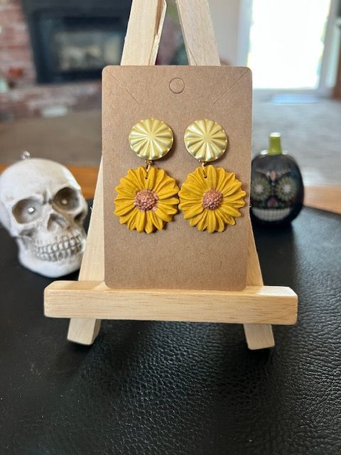 A pair of yellow sunflower earrings are sitting on a wooden easel.