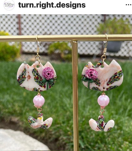 A pair of earrings are hanging on a gold display stand.