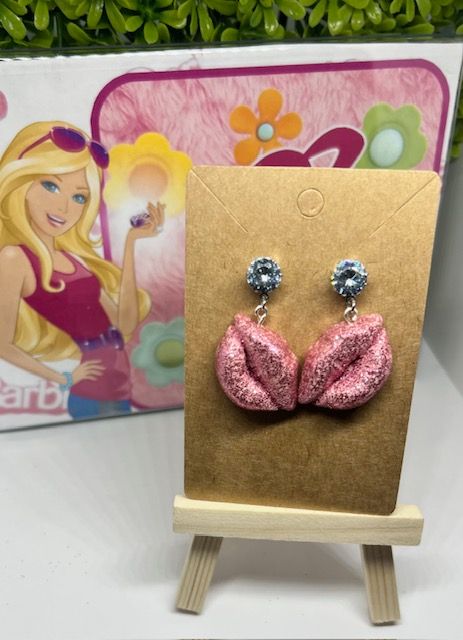 A pair of pink earrings are on display in front of a barbie box