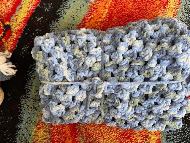A blue and white crocheted item is sitting on a colorful rug.