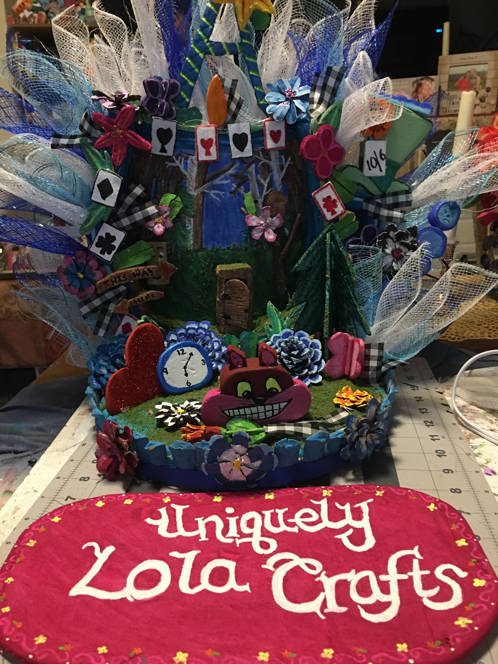 A fake cake gift basket  with a clock on top of it themed like Alice In Wonderland