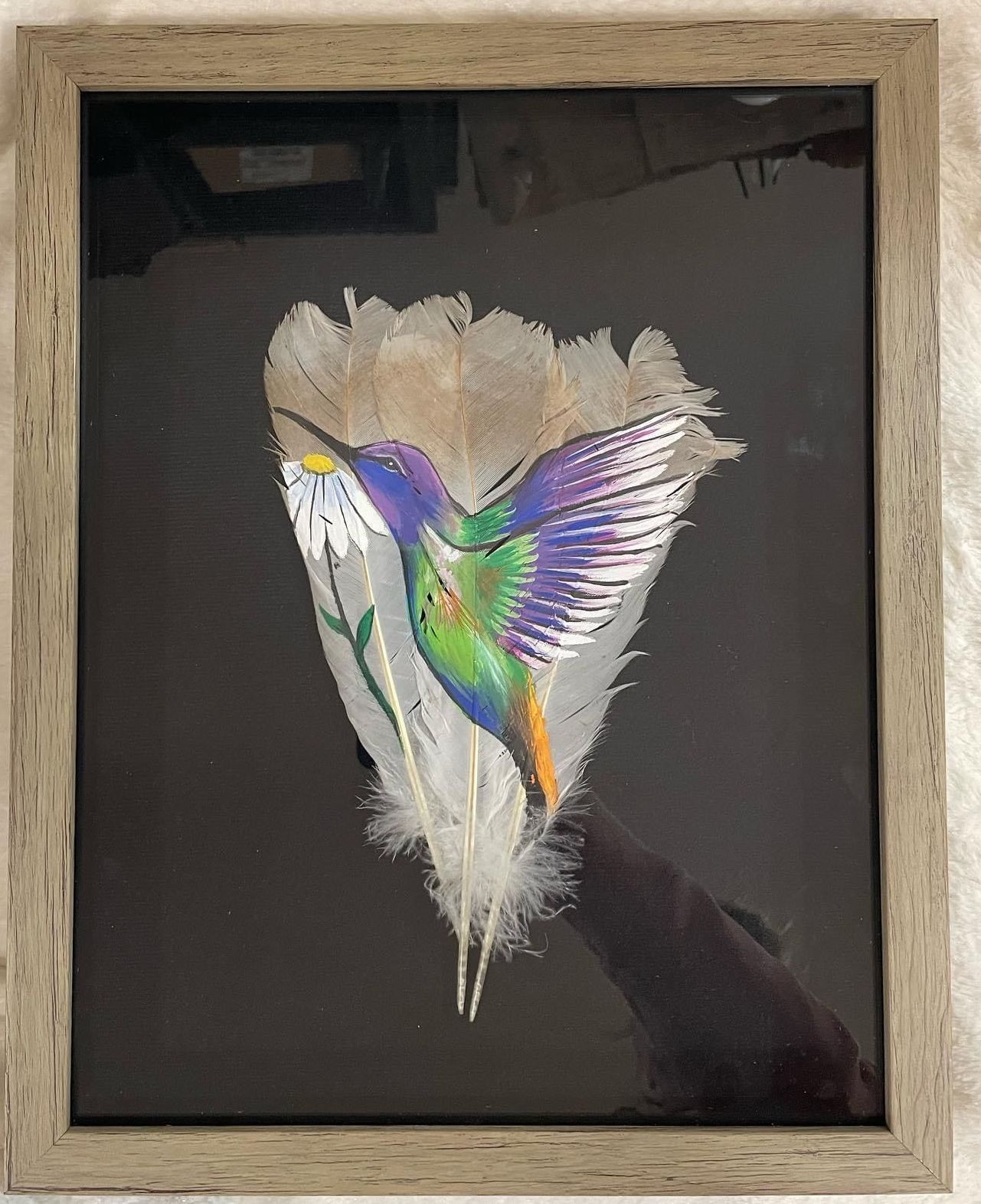 A picture of a hummingbird painted on a feather in a frame.