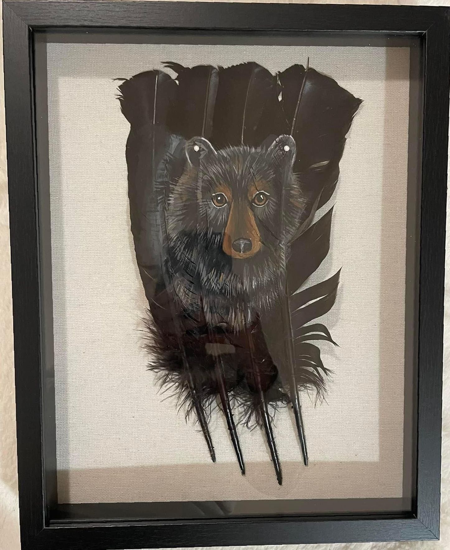 A black bear is sitting on a feather in a frame.