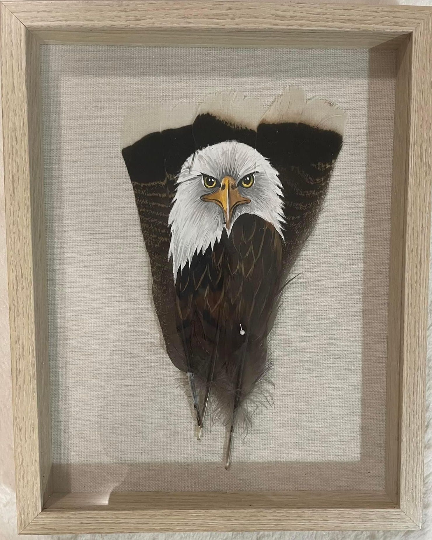 A bald eagle is painted on a feather in a wooden frame.