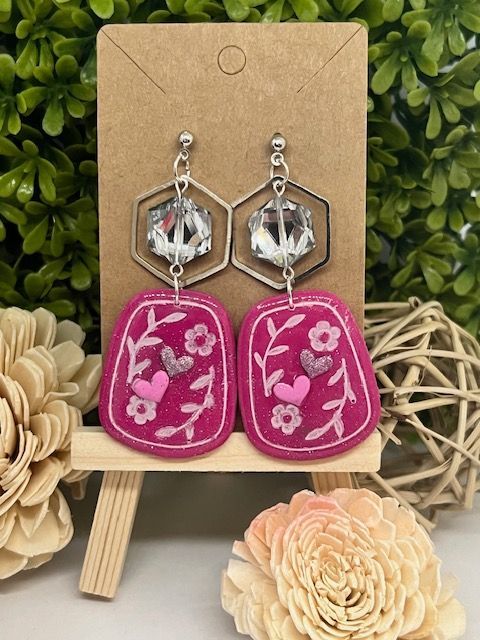 A pair of pink earrings are sitting on a cardboard holder.
