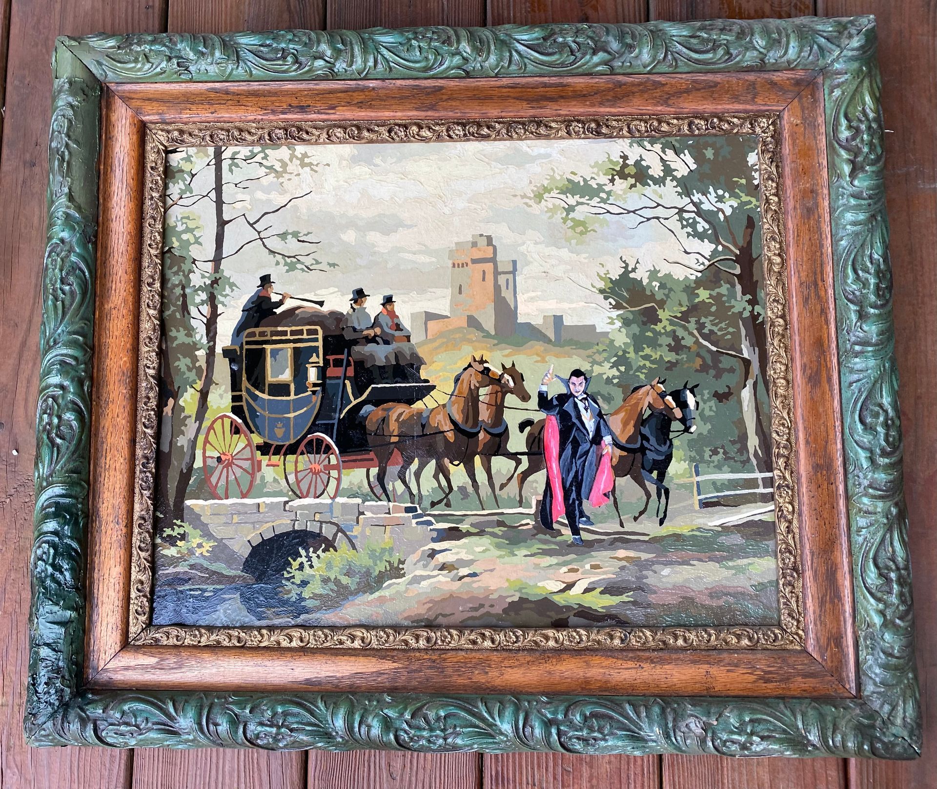 A framed painting of a horse drawn carriage on a wooden table.