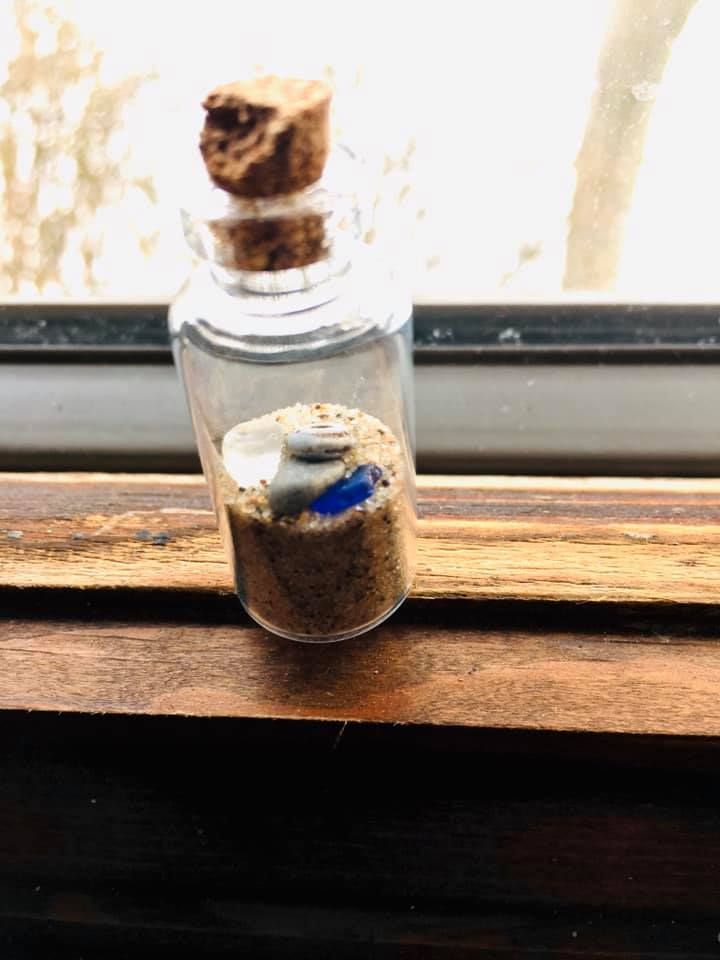 A small glass bottle filled with sand and a cork stopper is sitting on a wooden table.