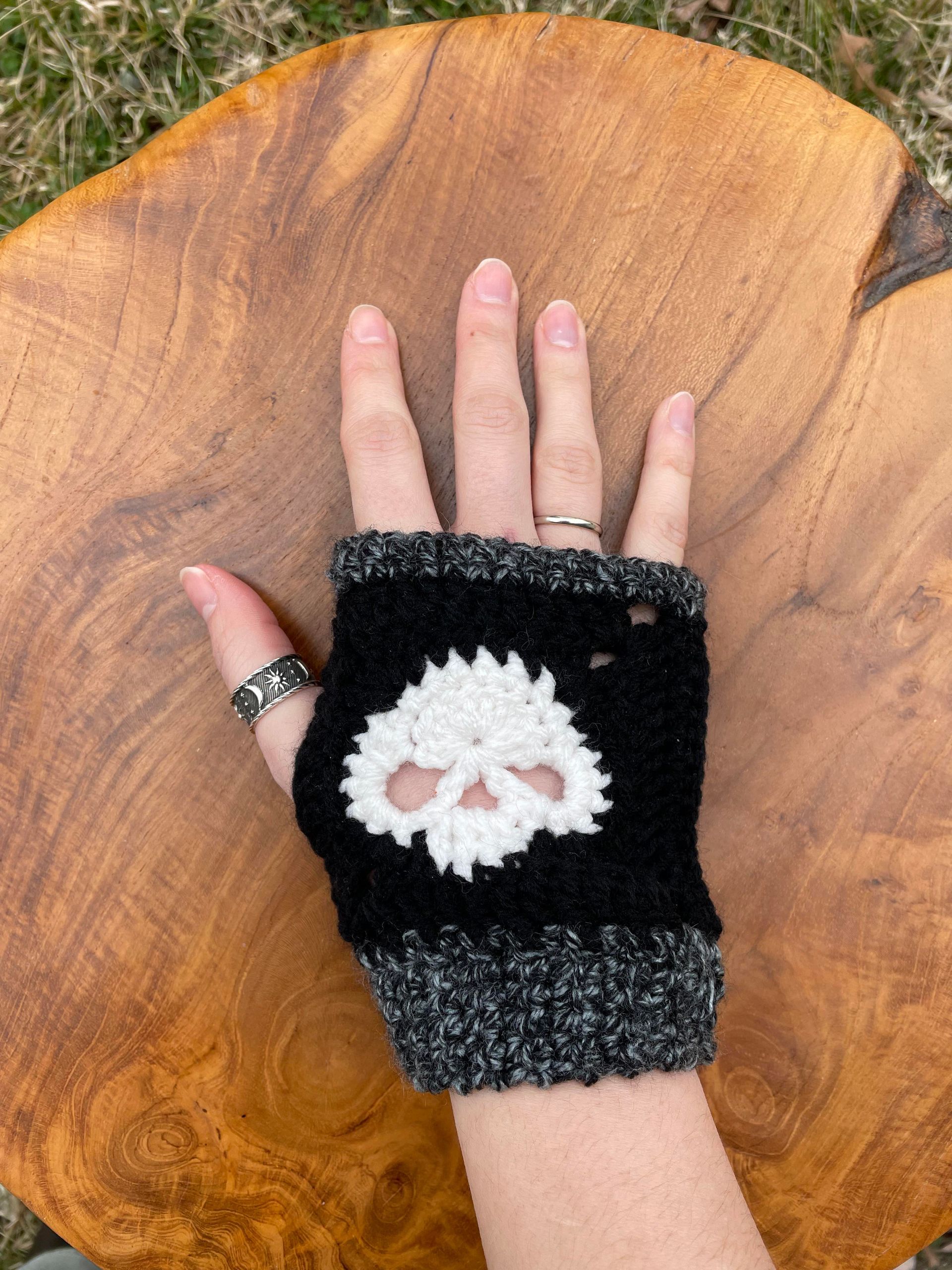A person is wearing a crocheted fingerless glove with a skull on it.