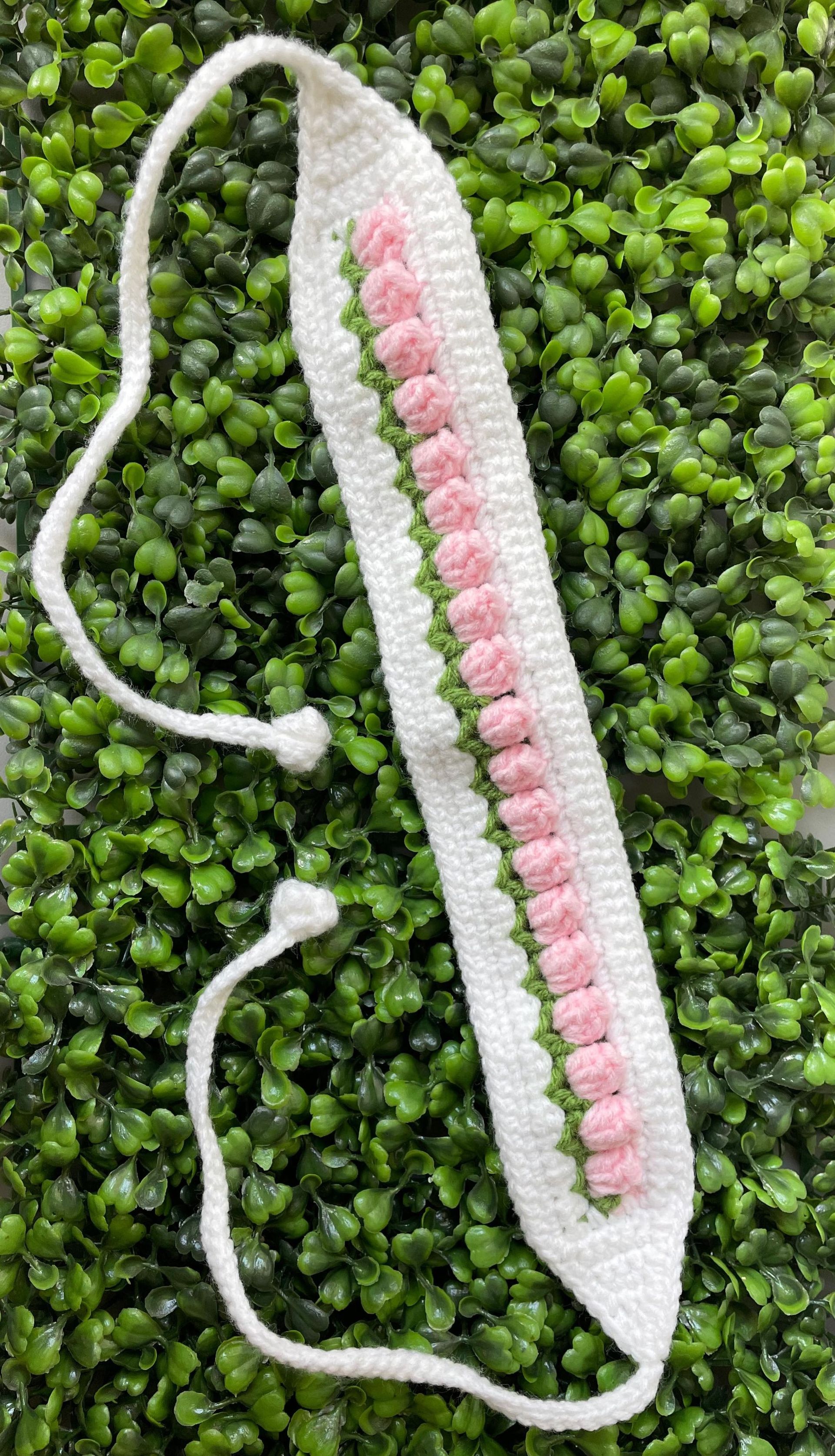 A white and pink crocheted headband is sitting on top of a green wall.