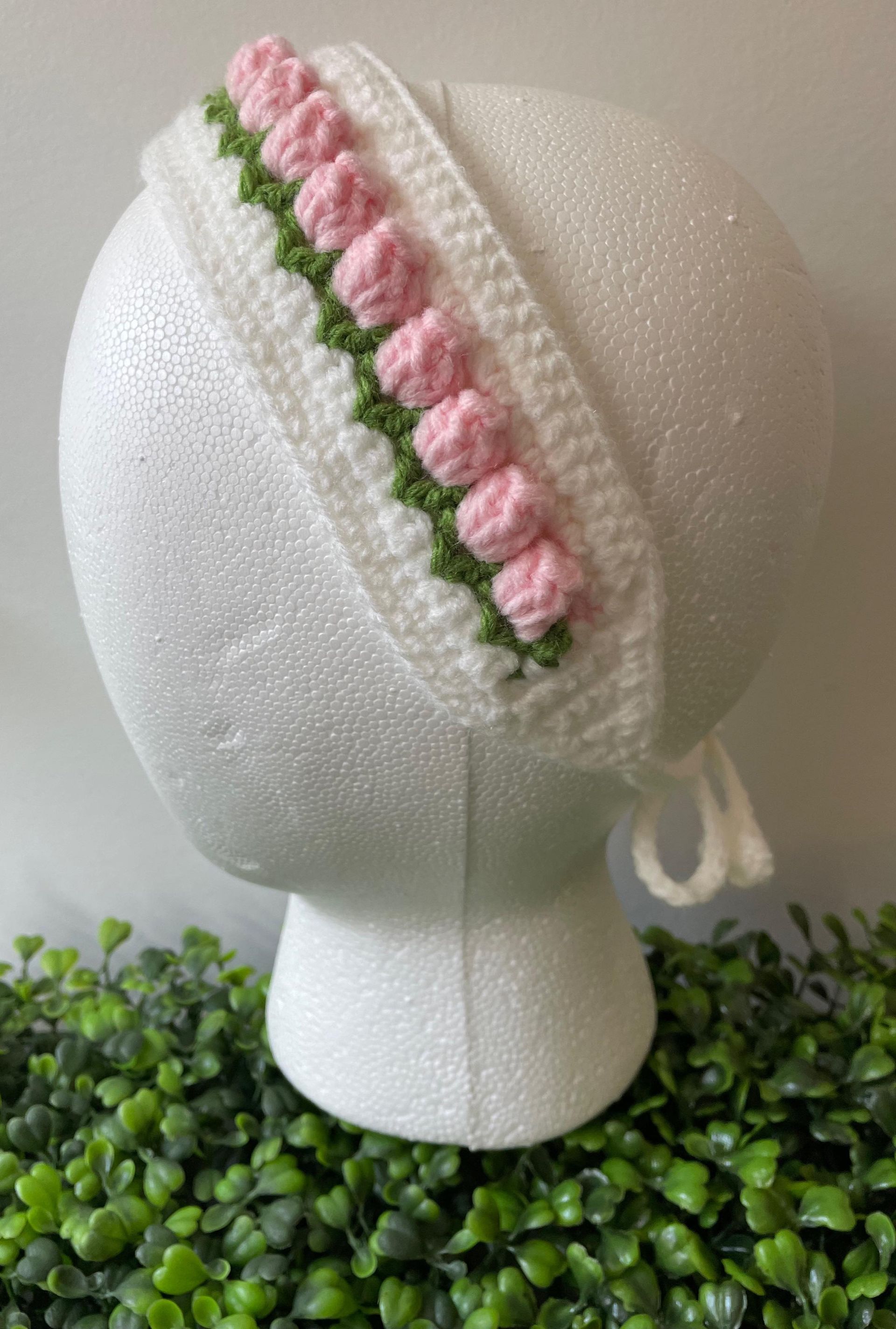 A white mannequin head with a pink and green crocheted headband on it.