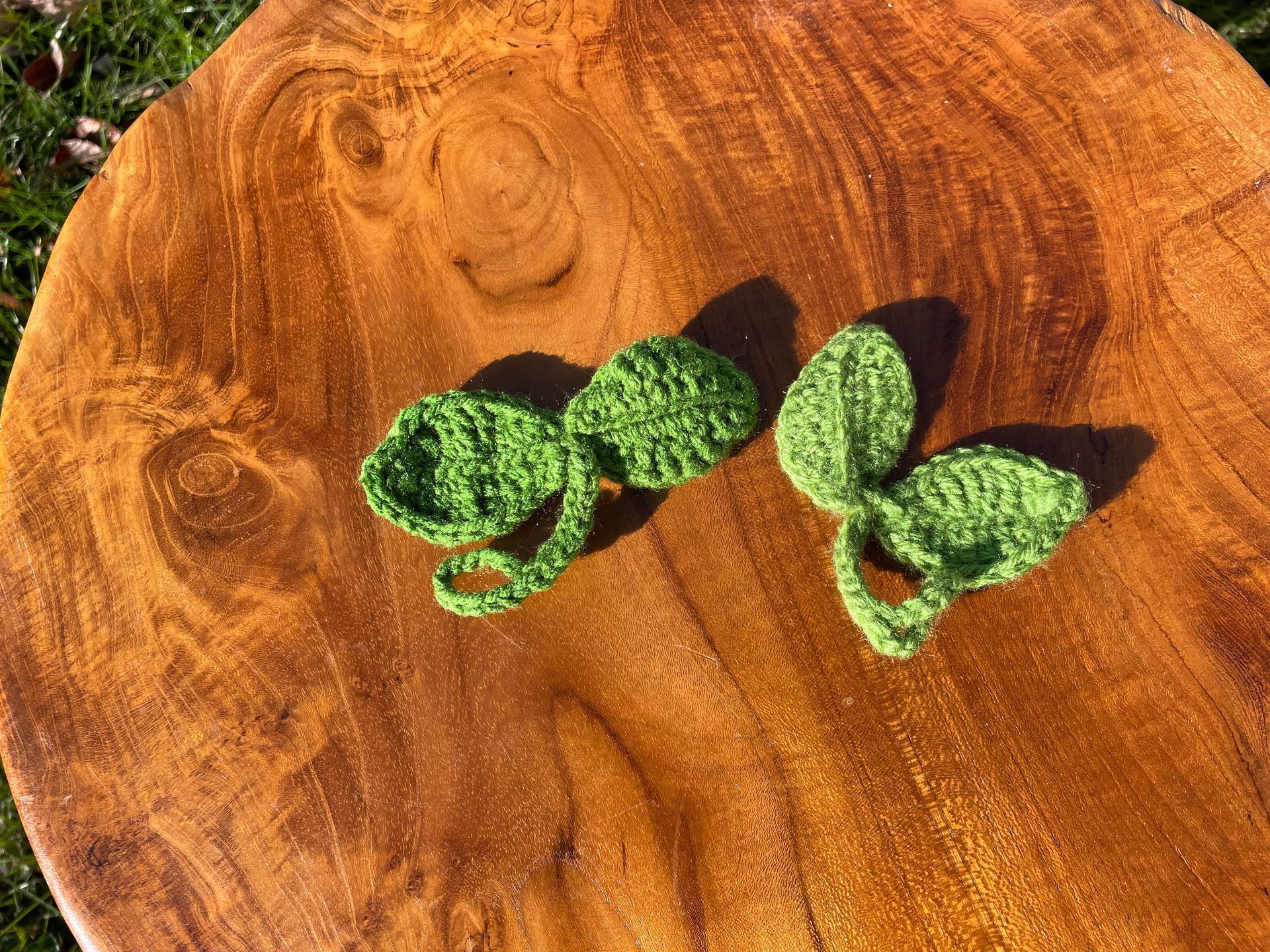 Two green crocheted leaves are sitting on top of a wooden cutting board.
