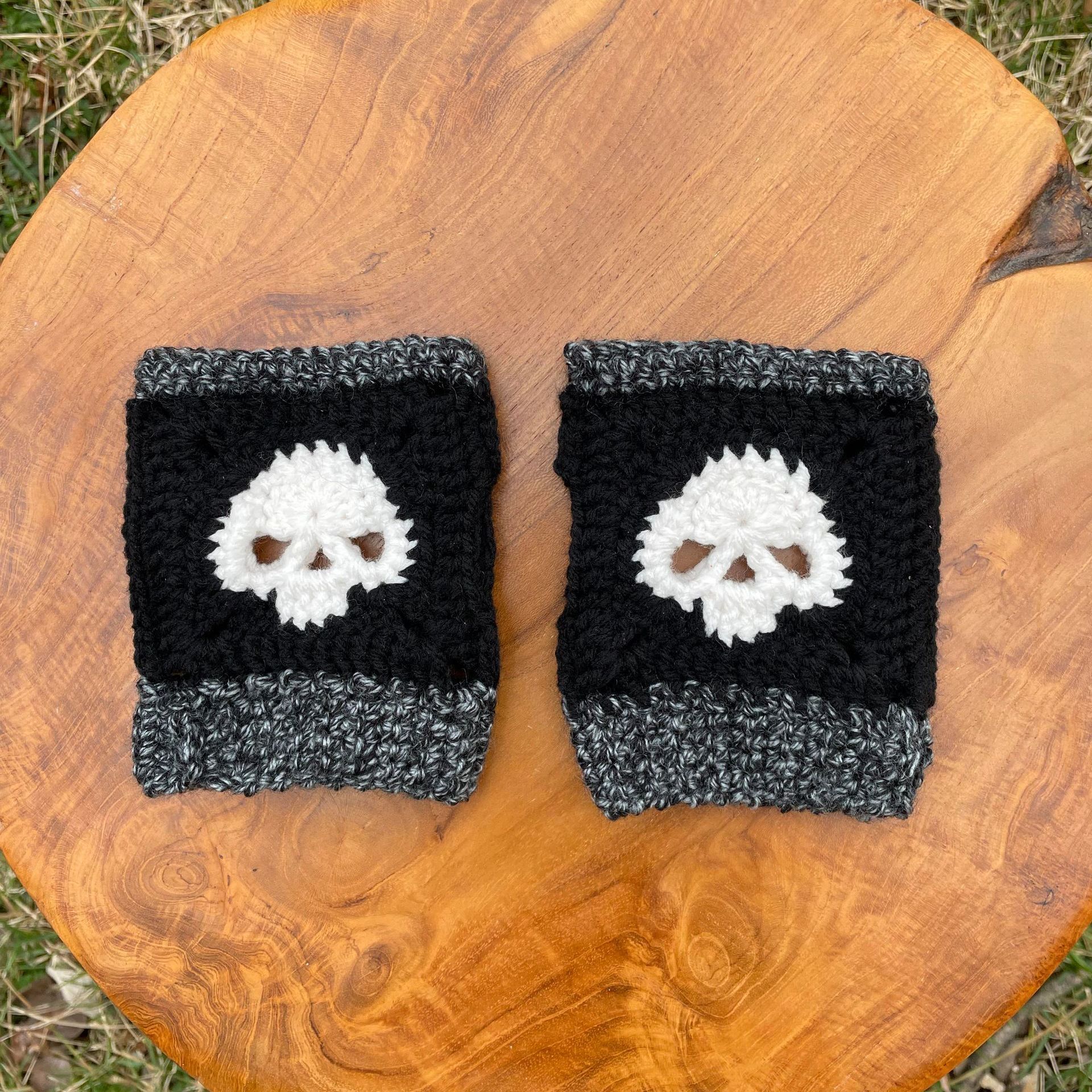 A pair of crocheted wrist warmers with skulls on them