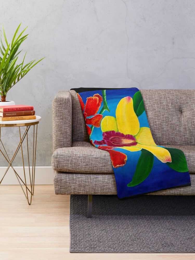 A colorful blanket with a yellow orchid on a blue background  is sitting on a couch in a living room.