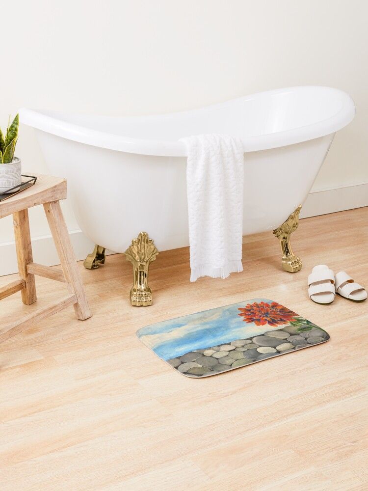 There is a bathtub in the bathroom with a rug showing original artwork called 