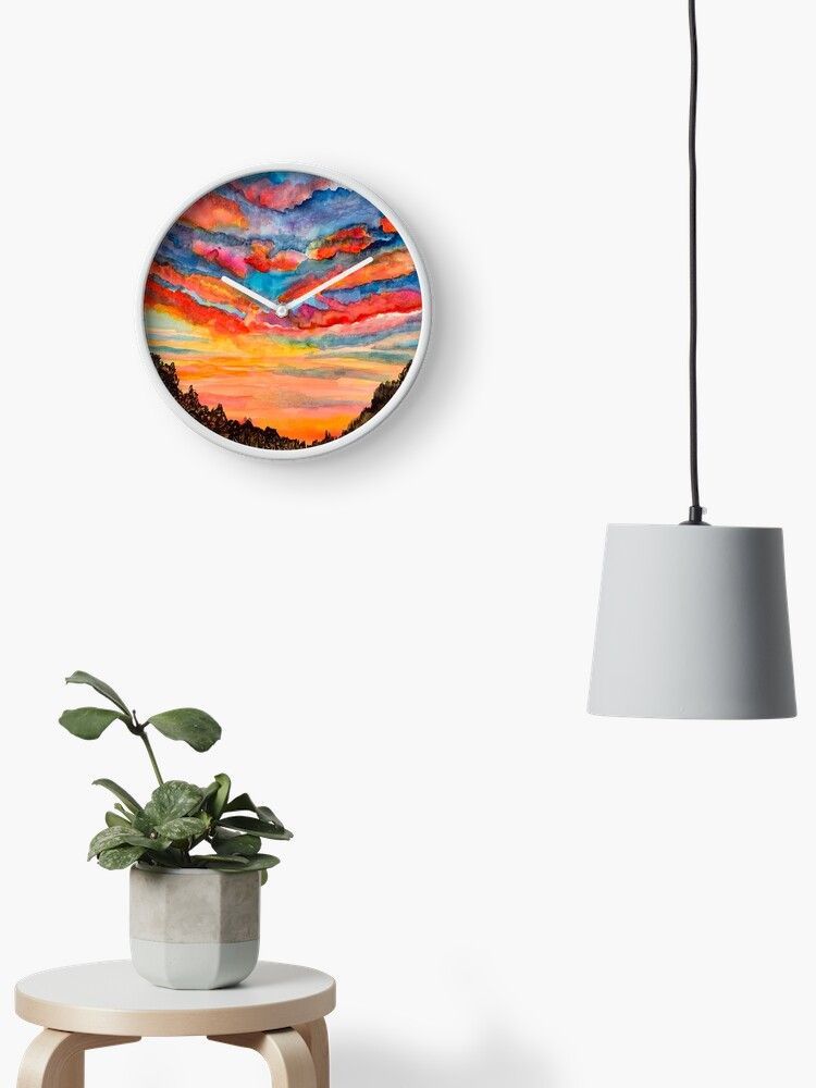 A clock is hanging on a wall next to a plant and a lamp.