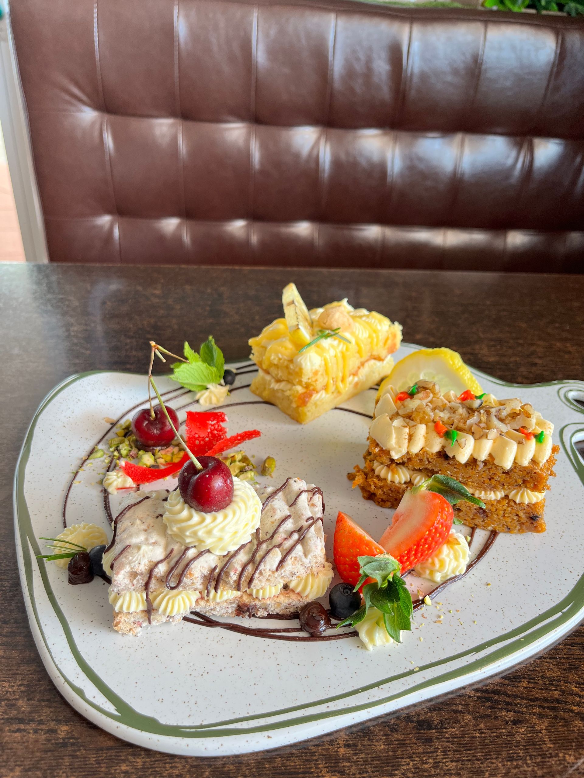 A platter with three small slices of cake, decorated with fresh cherries, a strawberry, lemon, and mint on a white plate - Café and Restaurant in Cannonvale, QLD