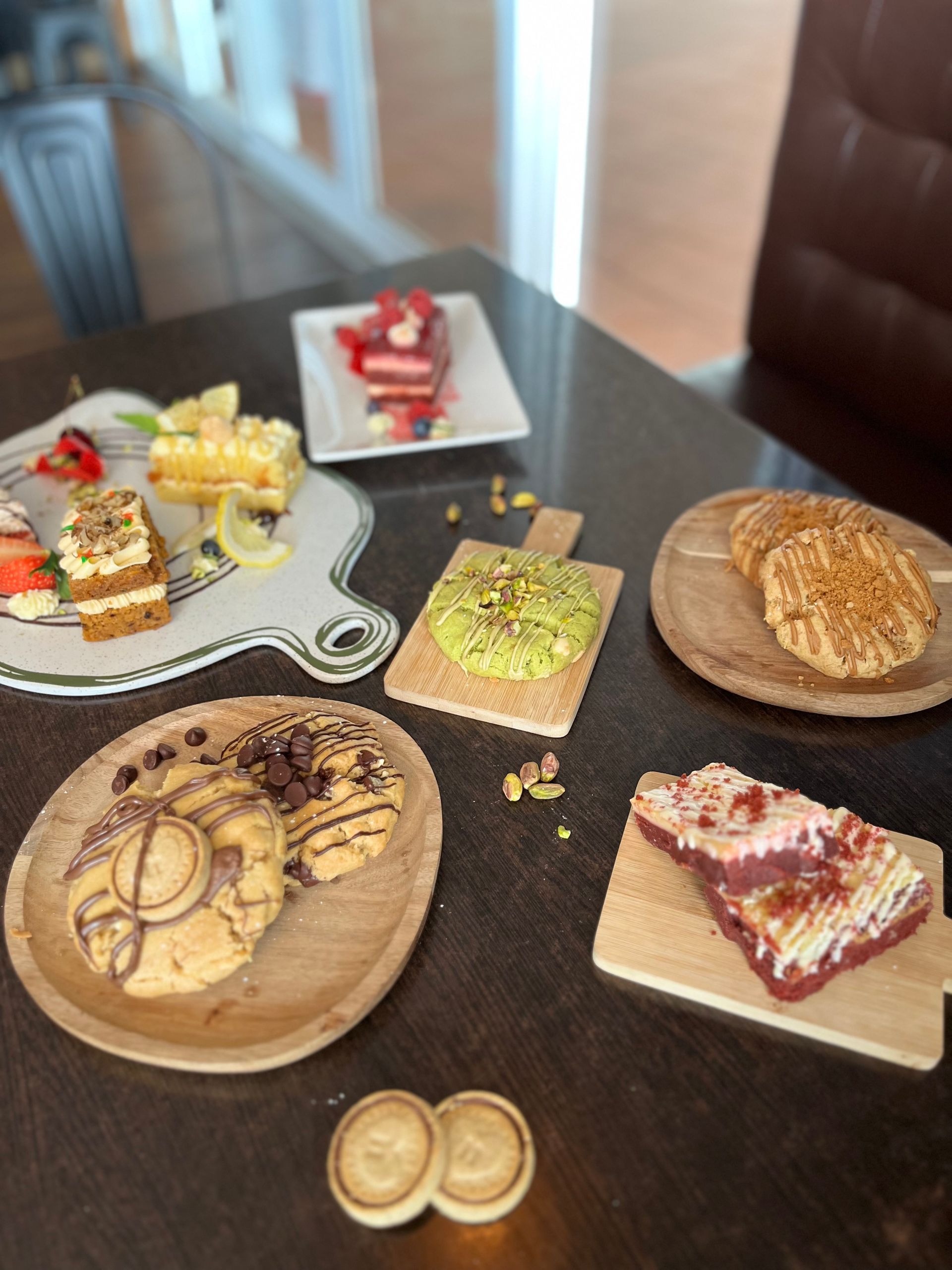 A table displays an assortment of pastries, cookies, and layered cakes on various plates and wooden boards - Café and Restaurant in Cannonvale, QLD