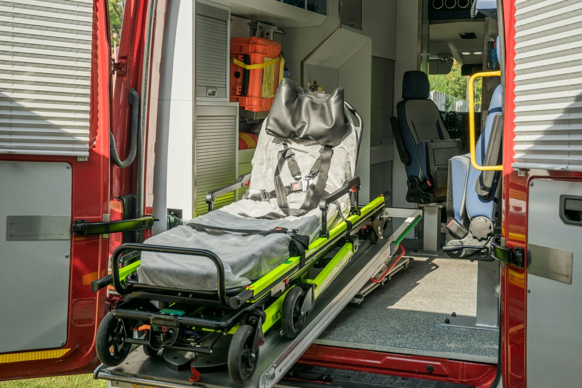 Inside an ambulance, a stretcher is on a ramp. The back doors are open.