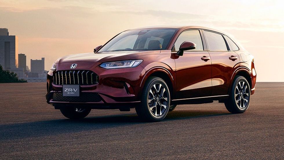 Um SUV vermelho escuro estacionado contra o horizonte da cidade ao pôr do sol.