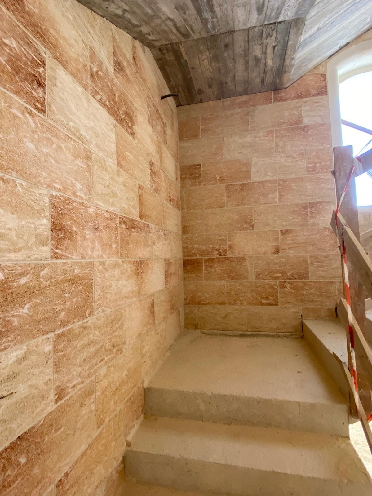 Una scala con ringhiera in legno e muro in pietra.